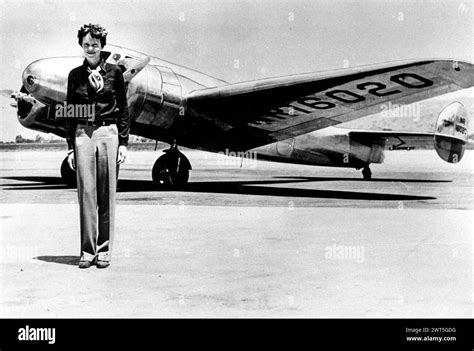 amelia earhart in pilot uniform standing beside lockheed electra nose section