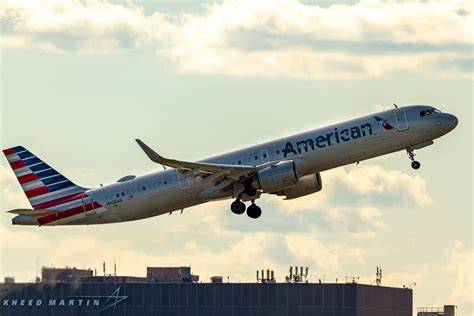 American Airlines Airbus A321neo taxiing on the JFK runway with terminal buildings behind