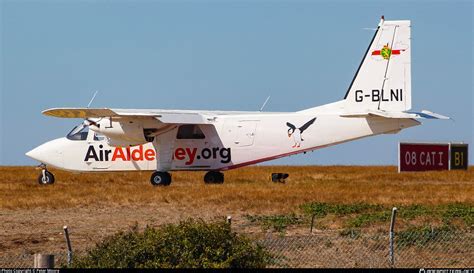 Britten-Norman Islander flying over remote island airstrip in Southeast Asia with volcanic terrain in background