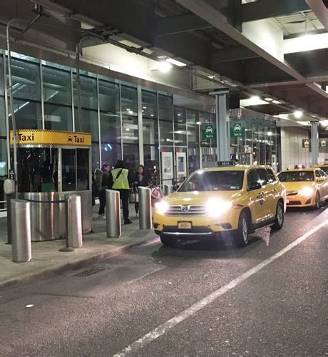 chauffeur-driven black sedan parked outside JFK Terminal 4 at night