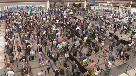 connecting passenger with rolling carry on bag walking through crowded airport security checkpoint queue