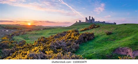dunstanburgh castle ruins on cliff edge above embleton bay at sunset