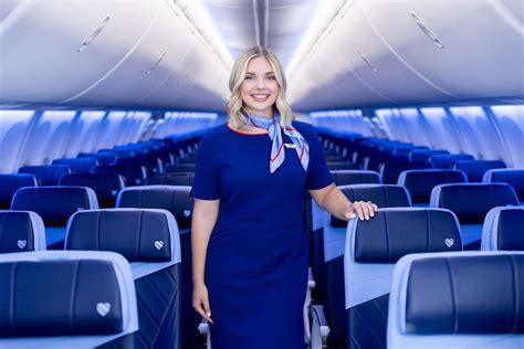 flight attendant in high-end uniform standing in private jet aisle with tablet in hand