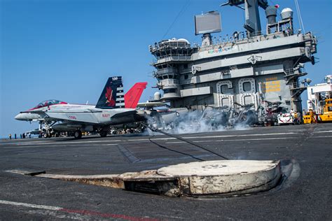 Four-star US Navy Admiral speaking aboard aircraft carrier with naval aviators nearby