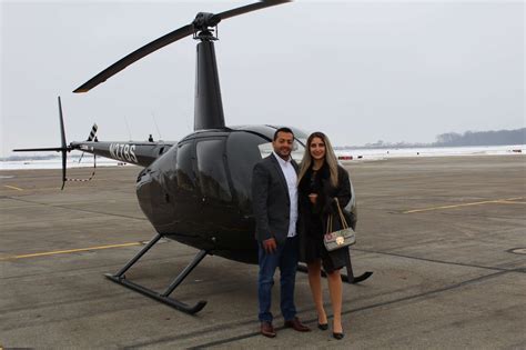 Happy couple post-proposal with R44 helicopter in background near Erie airfield