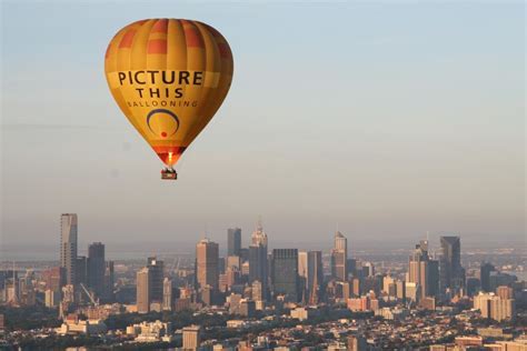 hot air balloon drifting above Melbourne skyline at sunrise