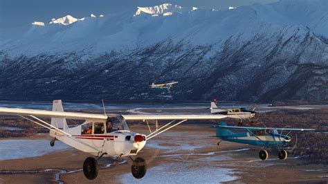 Small red and white bush plane parked on a remote Alaskan gravel river bar with mountains behind