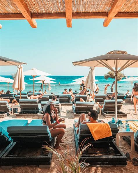 summer tourists relaxing at mykonos beach with yachts and sun umbrellas in view
