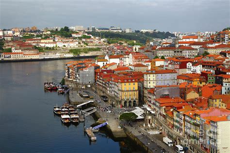 tourists walking through porto’s ribeira with aerial tram and douro river in background
