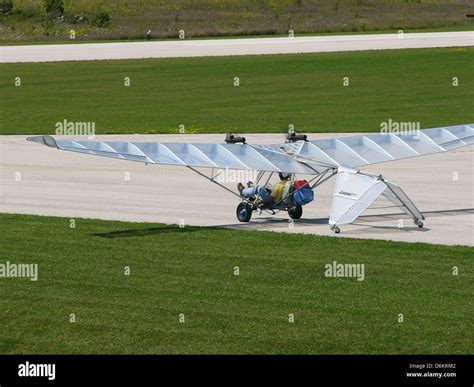 Two-seat ultralight-class aircraft landing at grass strip with sunset backdrop