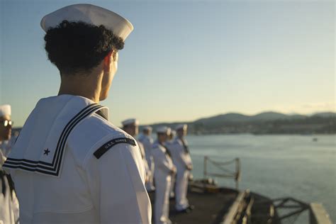 US Navy officer wearing wings of gold flight suit standing beside carrier-based fighter jet
