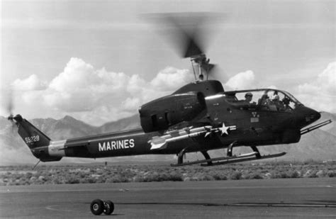 USMC AH-1J SeaCobra flying over coastal terrain with twin-engine nacelles visible