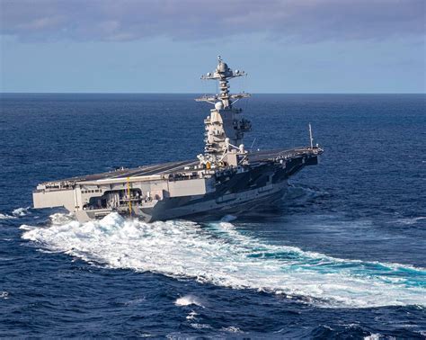 USS Gerald R. Ford CVN-78 conducting sea trials with F/A-18 Hornets on deck under sunset skies