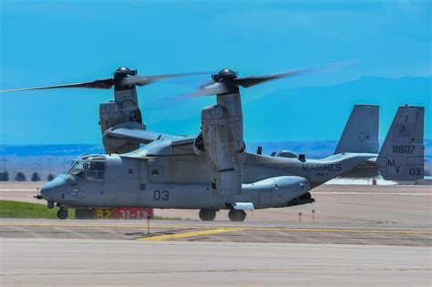v-22 osprey in mid-air rotor transition over desert terrain